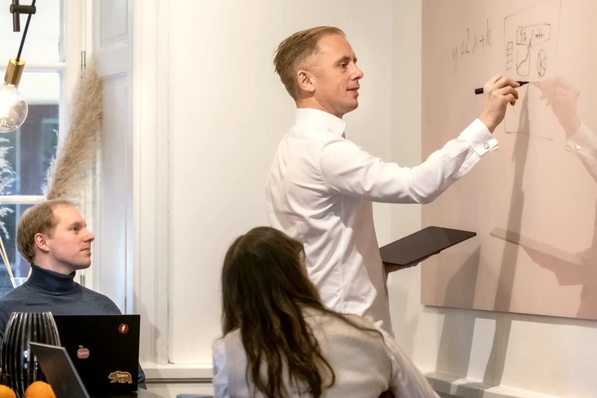Måns ritar på en whiteboard under ett möte medan två kollegor lyssnar